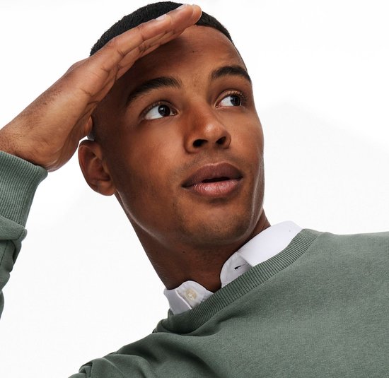 Close-up van een man met groene crewneck trui en wit overhemd.