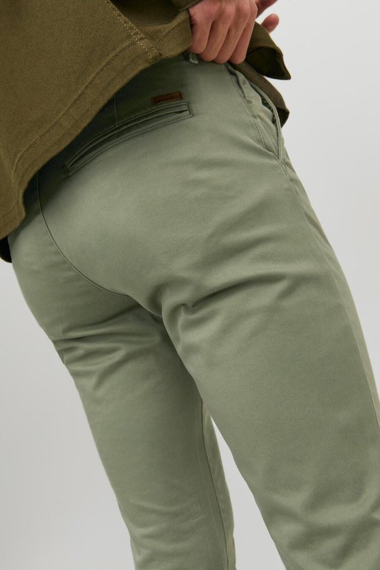 Detail van een smalle, lichtgroene broek met bruin label.