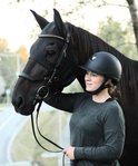 Vrouw in ruiterkleding staat naast een zwart paard dat een zwart Fenwick masker draagt.