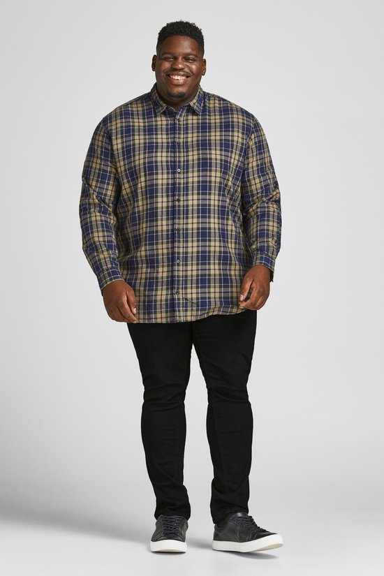 Man draagt een geruite blouse in blauw, beige en donkerblauw, met zwarte jeans.