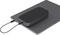 Donkergrijze powerbank ligt op een open laptop en wordt opgeladen via een USB-C kabel.