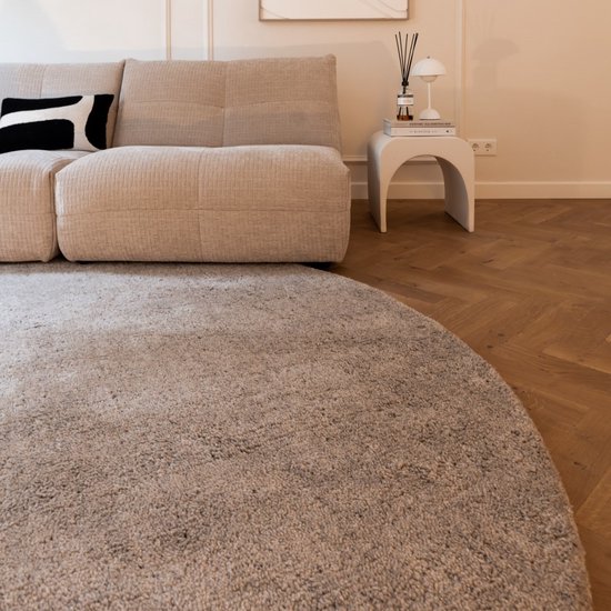 Rond, zandkleurig vloerkleed in een woonkamer, voor een beige bank.