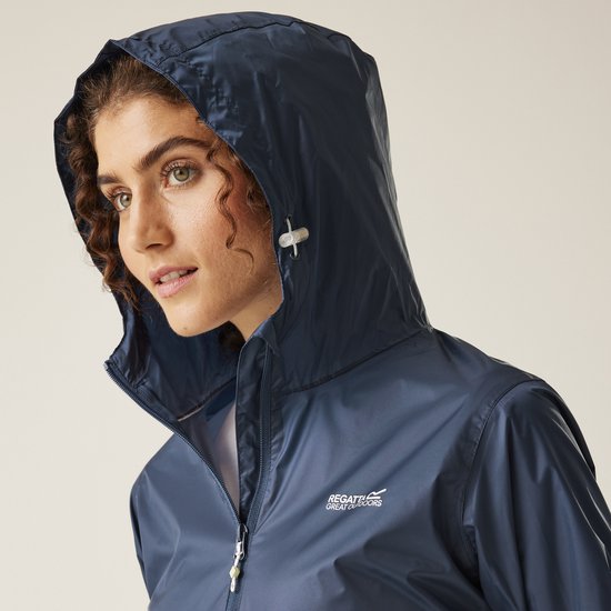 Close-up van een model met krullend haar dat de capuchon van een donkerblauwe regenjas omhoog doet.