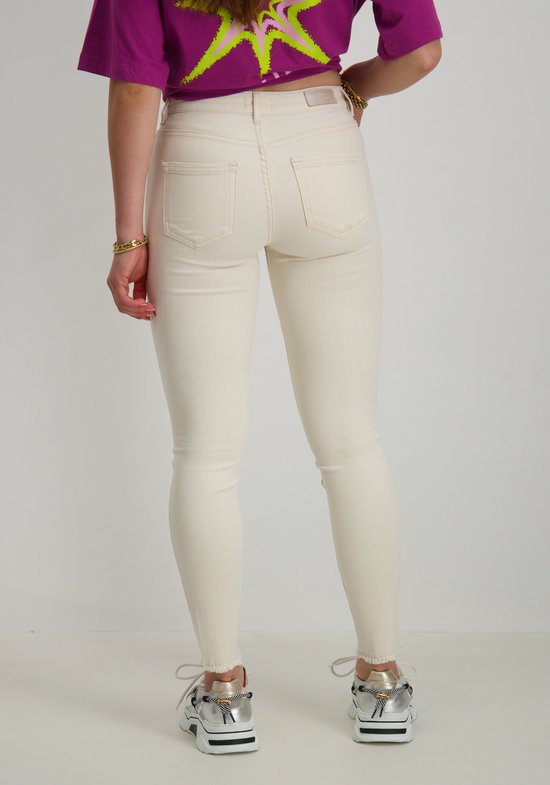 Achterkant van model in crème skinny jeans met paarse top en sneakers.