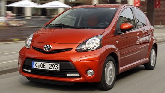 Oranje Toyota Aygo in beweging, van voren gezien.