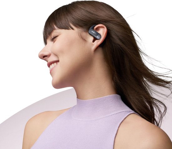 Femme aux yeux fermés porte un écouteur Shokz noir avec crochet d'oreille.