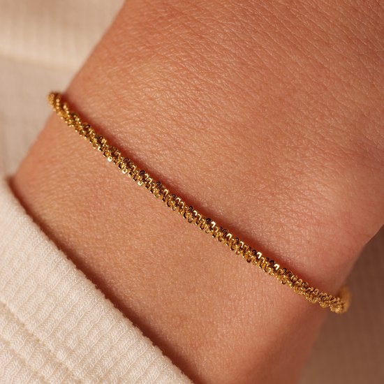 Damesarmband van goudkleurig staal met gedraaid patroon, gedragen om een pols.