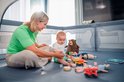 Vrouw en baby spelen in een grijze box met speelgoed.