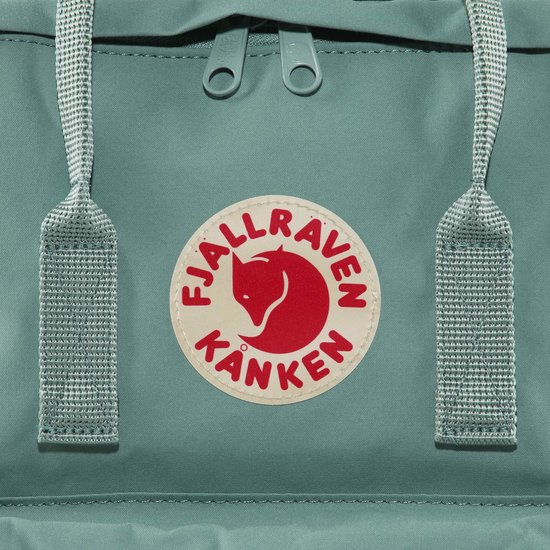 Close-up van het ronde logo op een turquoise Kånken rugzak.