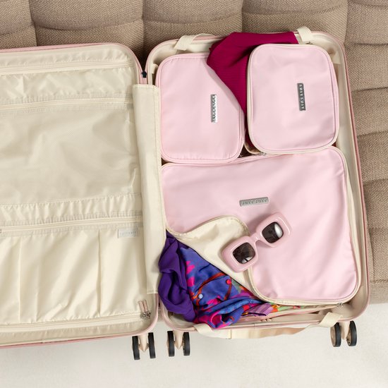 Een open roze pastel SUITSUIT koffer gevuld met packing cubes, een sjaal, zonnebril en kleding.