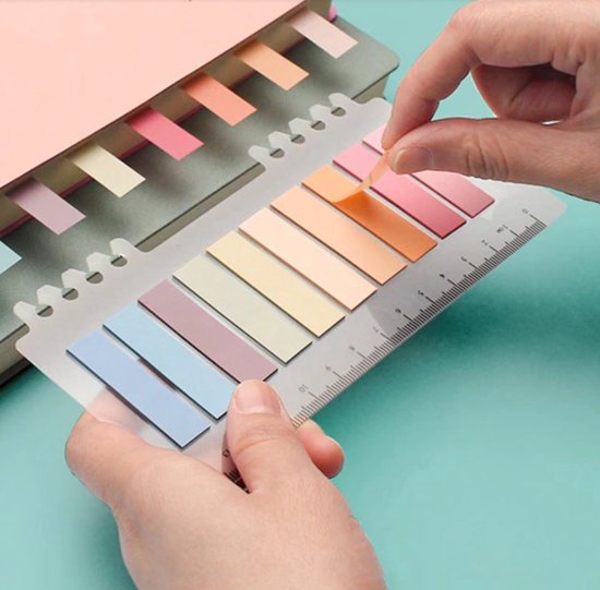 Handen die pastelkleurige index tabs met liniaal aanbrengen in een notitieboek.