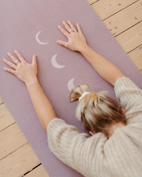 Een vrouw in een yogahouding op een lavendelpaarse mat met maanfasen.
