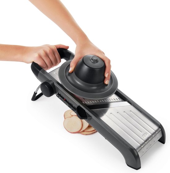Een mandoline met restenhouder, een aardappel wordt gesneden met gesneden aardappelschijfjes ernaast.