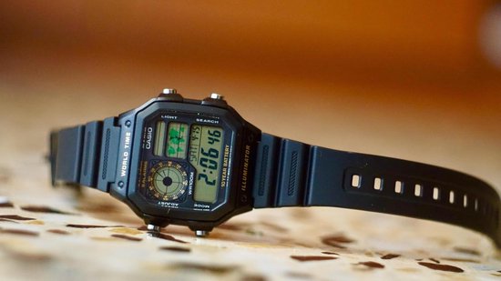 Zwarte Casio World Time horloge liggend op een getextureerd oppervlak.