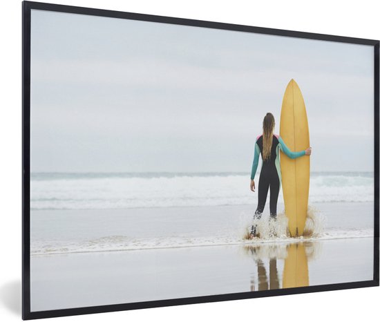 Photo encadrée - Surfeuse debout à côté du cadre photo planche de surf noir sans passe partout 120x80 cm - Affiche encadrée (Décoration murale salon / chambre)