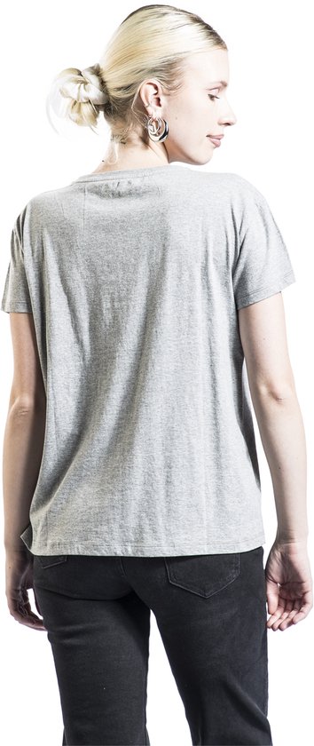 Grijs T-shirt, achterkant zichtbaar. Vrouw met blonde staart, grote oorbellen en zwarte jeans.