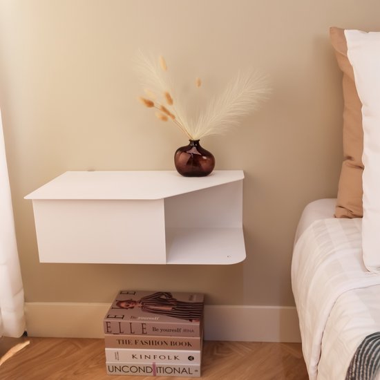 Witte wandplank met een bruine vaas met droogbloemen, naast een bed.