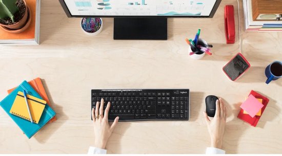 Perspectief van bovenaf op een bureau met een zwarte Logitech toetsenbord en muis, handen typen.