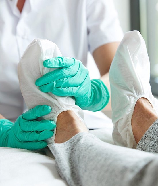 Een persoon met teal handschoenen plaatst witte Swash Foot Caps op beide voeten.