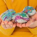 Kinderhanden houden drie grijze stenen vast, versierd met strass steentjes, zeesterren en bloemen.