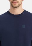 Close-up van donkerblauwe sweater met ronde hals en vierkant logo.