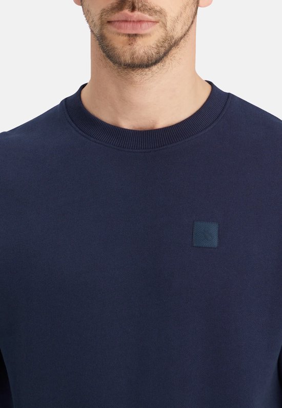 Close-up van donkerblauwe sweater met ronde hals en vierkant logo.