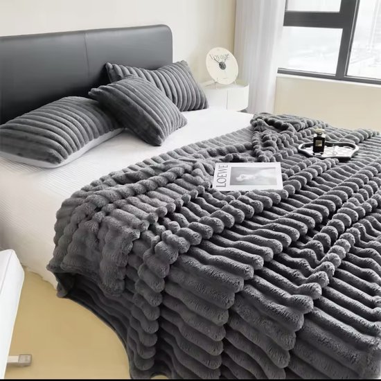 Grijze deken met verticale ribbels op een bed met kussens en een tijdschrift.
