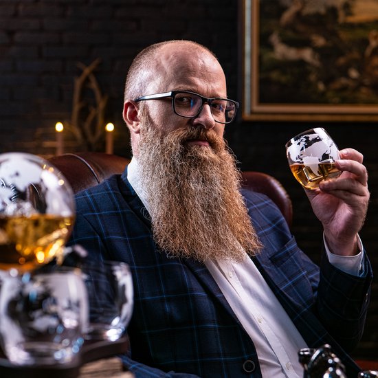 Man met baard en bril, houdt glas in de hand met wereldbol-opdruk. Jas met blauwe ruit.