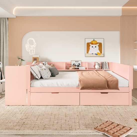 Roze slaapbank met twee lades, boekenplanken en bureau, opgemaakt met kussens.