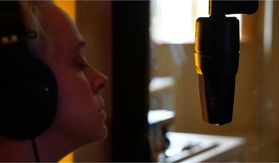 Vrouw met koptelefoon zingt in een studio, dichtbij een sE Electronics microfoon.