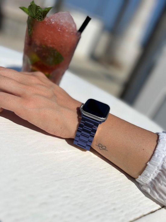 Draagster met blauw metalen Apple Watch bandje en Apple Watch, met cocktail op de achtergrond.