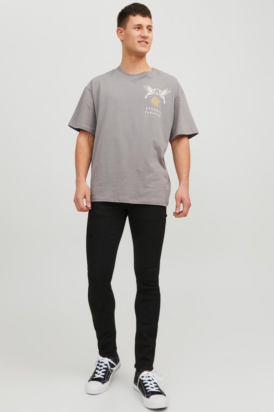 Man met grijze t-shirt met 'Eternal Paradise' print, zwarte skinny jeans en zwart-witte sneakers.