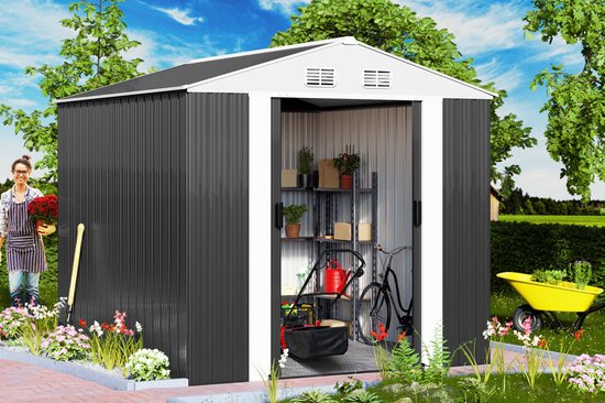 Een vrouw met een schort en bloemen staat naast een donkergrijs metalen tuinhuis in een tuin met een gele kruiwagen.