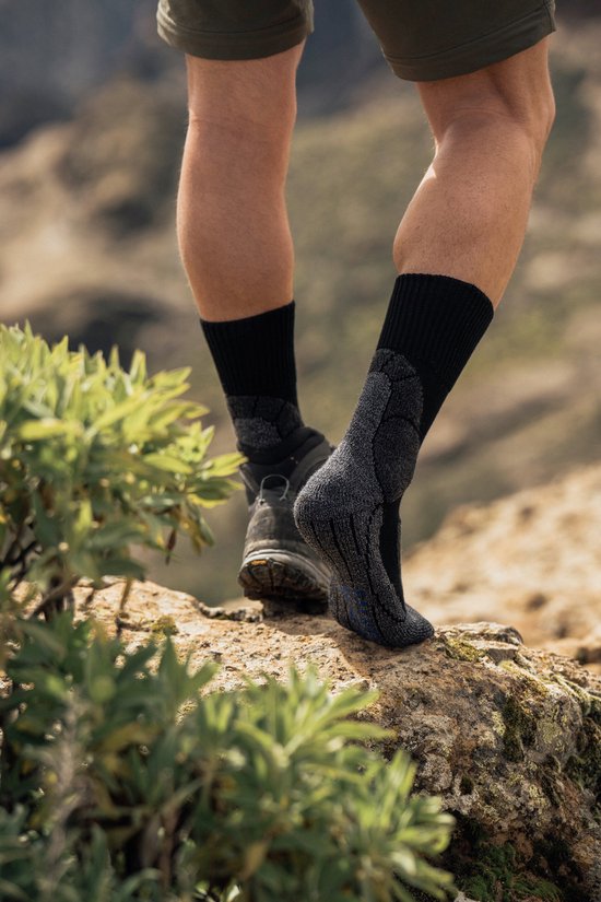Gezichtspunt van achteren: benen in zwarte wandelsokken met grijze accenten, naast een zwarte wandelschoen.