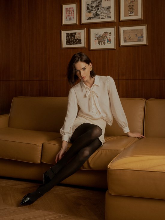 Model met zwarte, semi-transparante panty zittend op een bank.