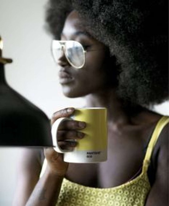 Vrouw met afro-kapsel en grote bril, vasthoudend een lichtgele mok met witte onderkant.