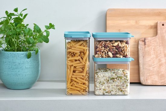Trois boîtes de conservation transparentes avec couvercles turquoise; une remplie de penne, une de mélange de riz, une de noix.