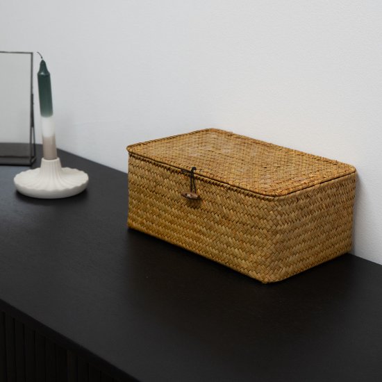 Une boîte de rangement en rotin marron clair avec couvercle et fermeture à bouton en bois est posée sur une commode noire.