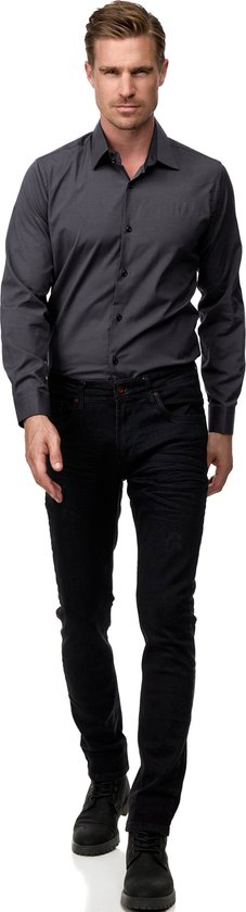 Man loopt naar voren in een donkergrijs overhemd en zwarte jeans.