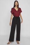 Model in bordeauxrode top met V-hals en wijde, zwarte broek met strikceintuur.