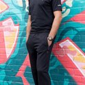 Man draagt een zwarte joggingbroek met ritsvak, staand voor een graffitikunstwerk.