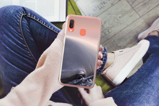 Persoon met spijkerbroek en roze trui houdt telefoon vast met dolfijnhoes.