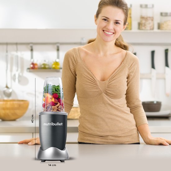 Vrouw in keuken staat naast Nutribullet blender, met afmetingen.