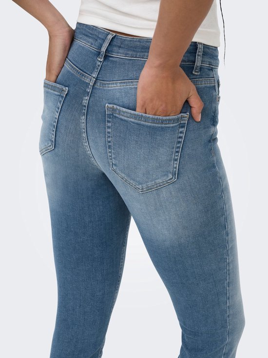 Close-up van de achterkant van een blauwe skinny fit jeans, met handen in de achterzakken.