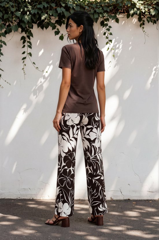 Model in bruine T-shirt en wijde broek met grote witte en bruine tropische bloemenprint.