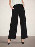 Model draagt zwarte wijde broek met hoge taille en een lichtgroen shirt.