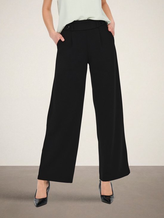 Model draagt zwarte wijde broek met hoge taille en een lichtgroen shirt.