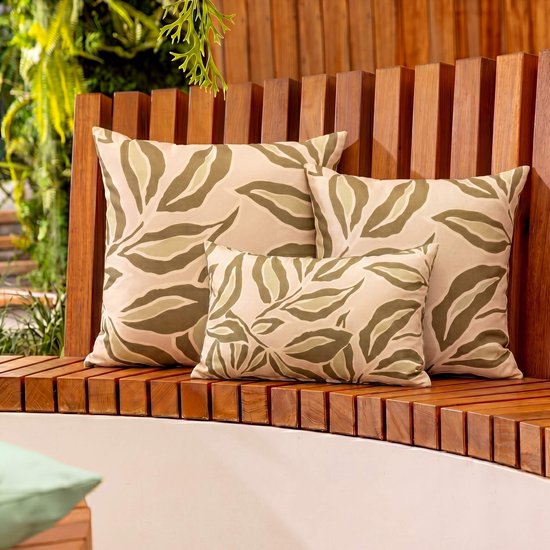 Drie kussens met bladmotief in beige en groen, op een houten bankje.