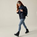 Model met rood haar loopt met een donkerblauwe regenjas, legging en rugzak.