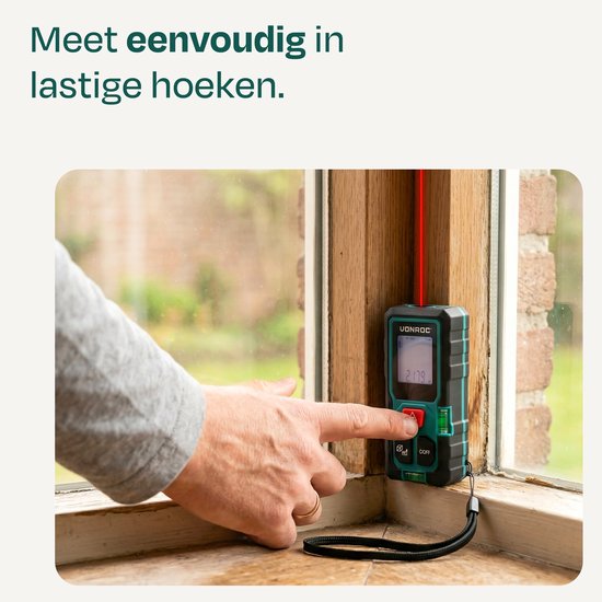 Hand drukt op de VONROC laser afstandsmeter die een rode laserstraal uitzendt naar een houten kozijn.